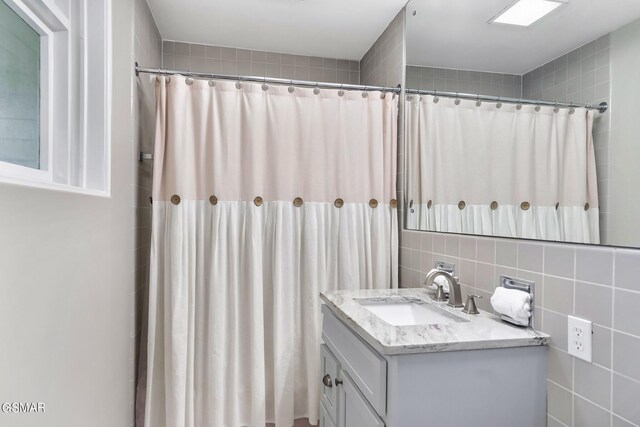 bathroom featuring decorative backsplash, vanity, tile walls, and walk in shower