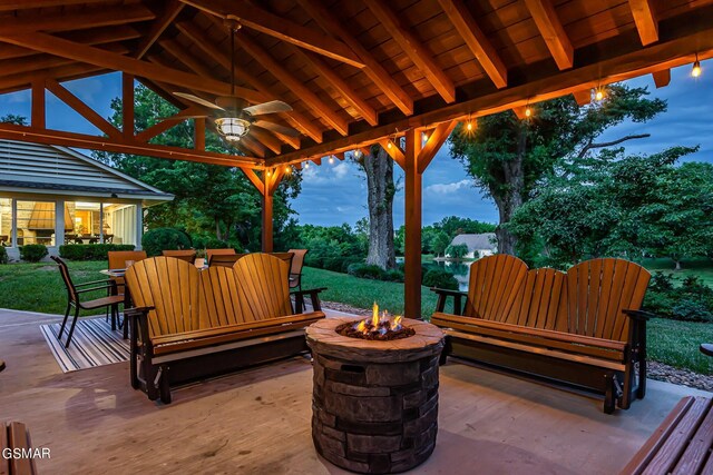 patio terrace at dusk featuring a fire pit, ceiling fan, and a lawn