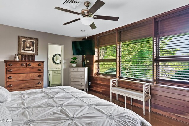 bedroom featuring wood walls, ensuite bathroom, and ceiling fan