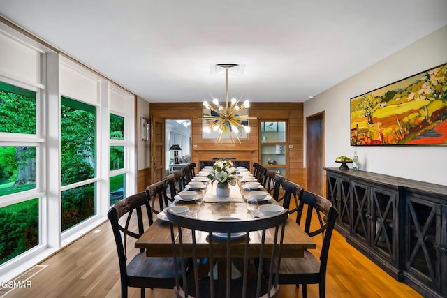 dining area featuring light wood-type flooring, an inviting chandelier, and wooden walls