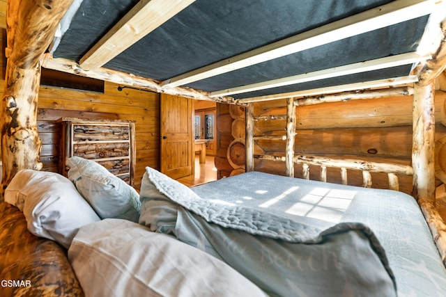 bedroom featuring log walls, beam ceiling, and wood finished floors