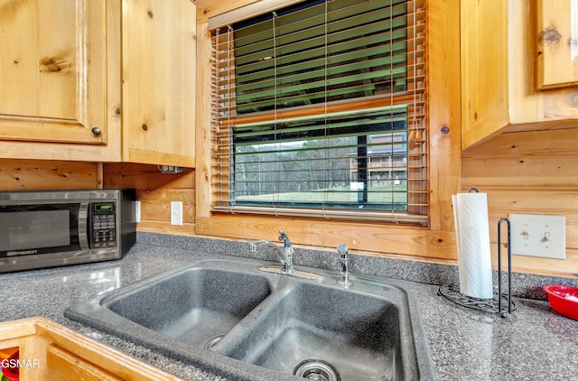 details featuring dark countertops, stainless steel microwave, light brown cabinets, wood walls, and a sink