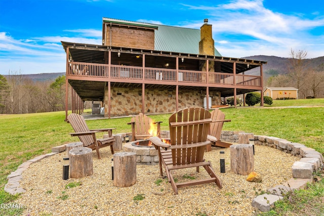 back of house featuring metal roof, stone siding, a yard, and an outdoor fire pit