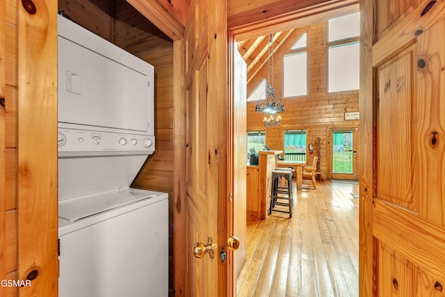 clothes washing area featuring wooden walls, laundry area, stacked washer and clothes dryer, a high ceiling, and light wood-style floors