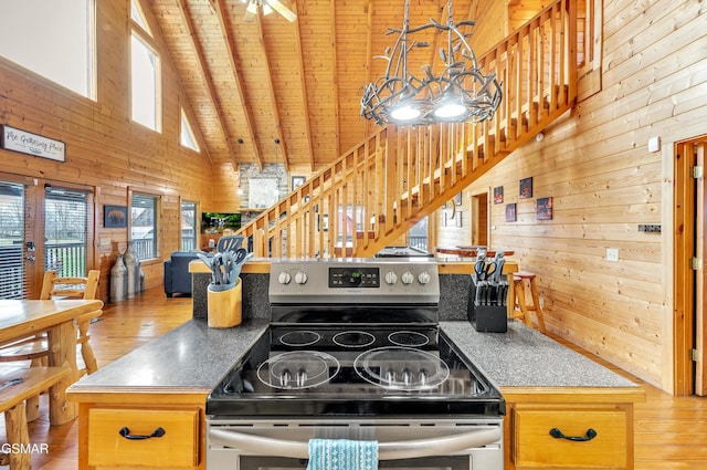 kitchen featuring wooden walls, wood ceiling, stainless steel electric range, wood finished floors, and high vaulted ceiling