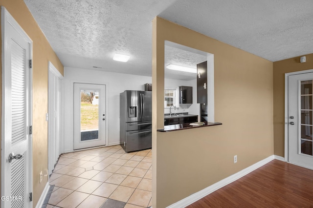 kitchen with light tile patterned floors, a textured ceiling, a sink, baseboards, and stainless steel fridge