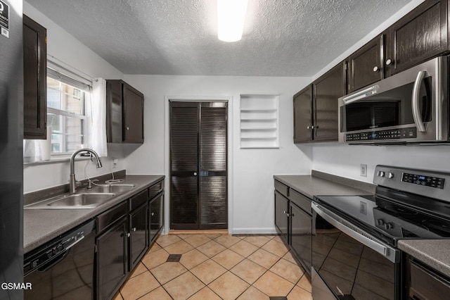 kitchen featuring stainless steel appliances, dark countertops, light tile patterned flooring, a sink, and a textured ceiling