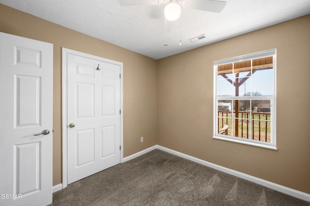 unfurnished room featuring visible vents, dark carpet, a textured ceiling, and baseboards