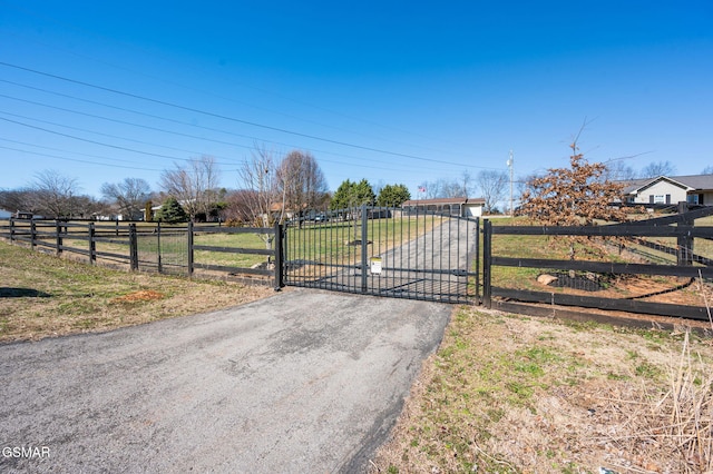 view of gate with a yard, a rural view, and fence