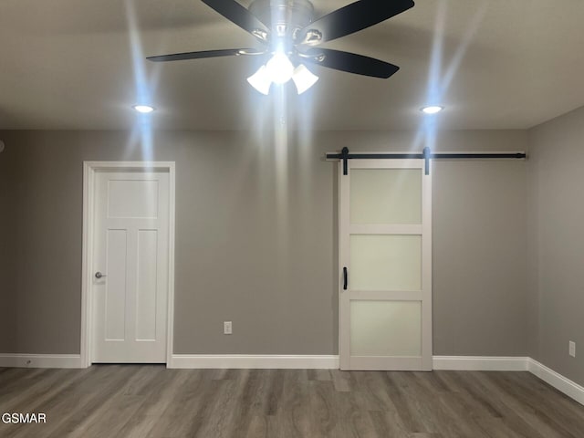 unfurnished bedroom with hardwood / wood-style flooring, ceiling fan, and a barn door