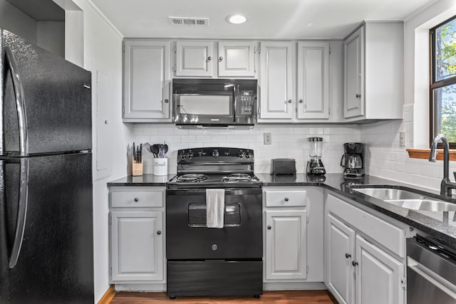 kitchen with sink, black appliances, dark stone counters, and tasteful backsplash