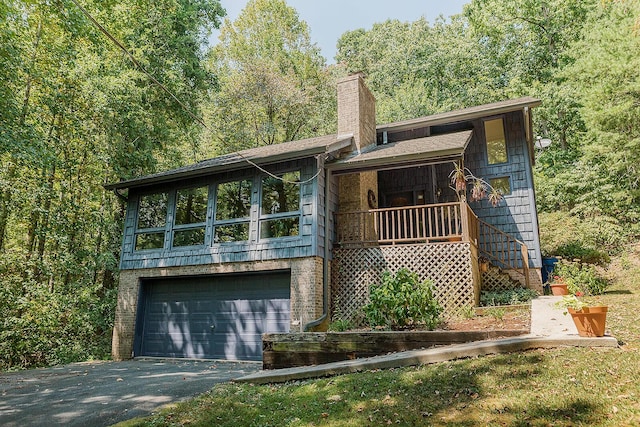 view of front of home with aphalt driveway, a chimney, an attached garage, and a view of trees