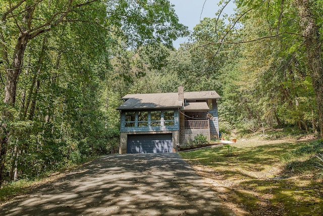 view of front of home featuring a chimney, driveway, a view of trees, and an attached garage