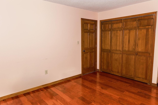 unfurnished bedroom with a textured ceiling, dark wood-type flooring, a closet, and baseboards