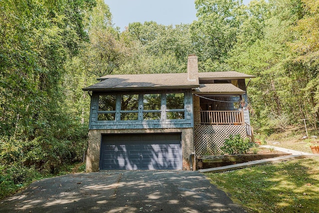 view of front of house featuring brick siding, a chimney, a view of trees, a garage, and driveway