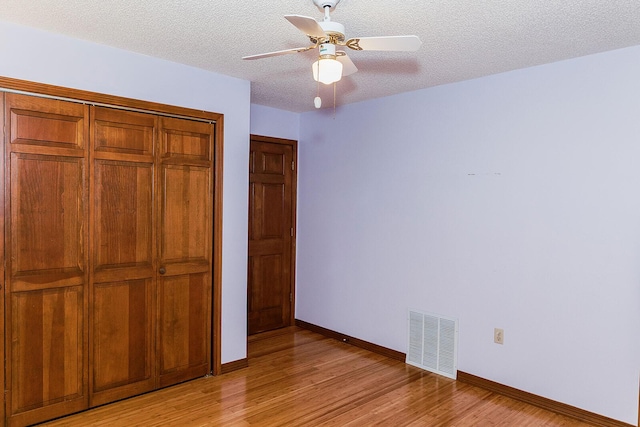 unfurnished bedroom featuring a textured ceiling, light wood-style flooring, visible vents, baseboards, and a closet