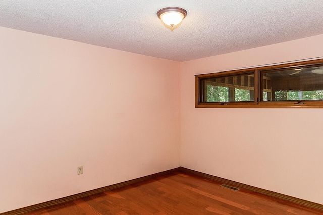 empty room with visible vents, baseboards, dark wood finished floors, and a textured ceiling