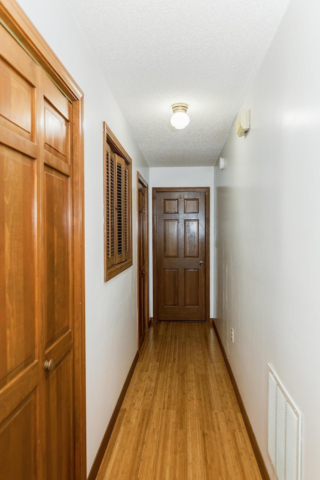 hallway featuring light wood-type flooring, baseboards, visible vents, and a textured ceiling