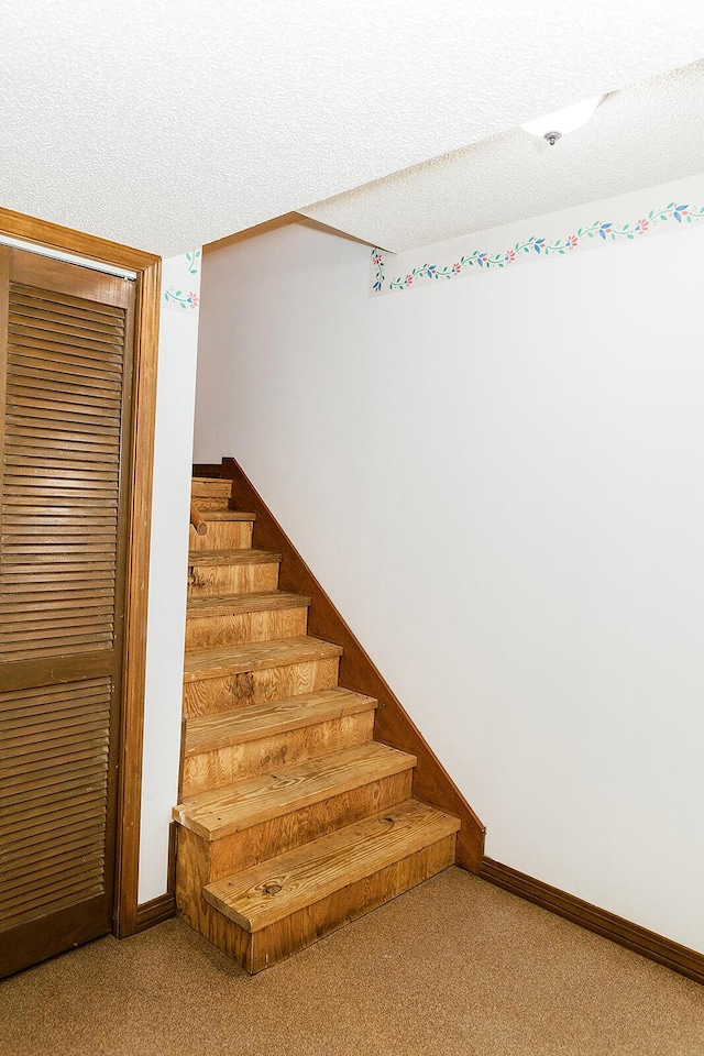 staircase featuring a textured ceiling, carpet floors, and baseboards