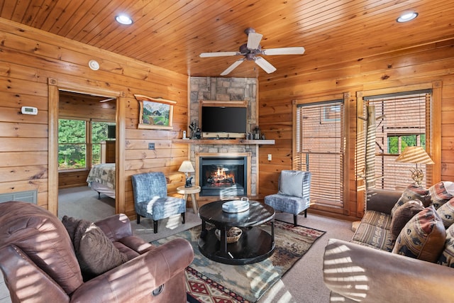 carpeted living room with ceiling fan, a fireplace, wood ceiling, and wooden walls