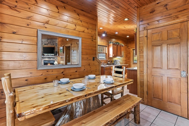 dining space featuring wood walls, a stone fireplace, wooden ceiling, and light tile patterned flooring