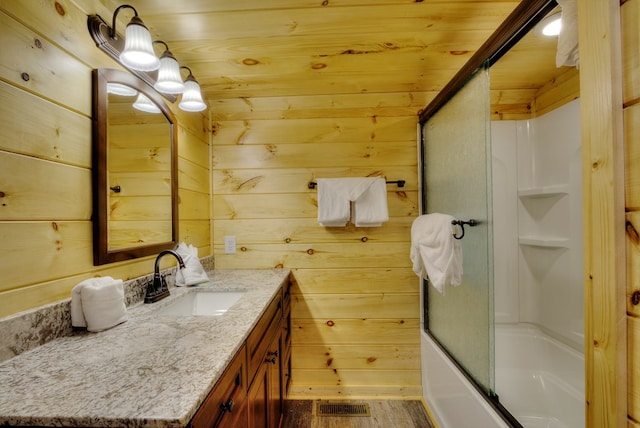 bathroom featuring wood walls, vanity, bath / shower combo with glass door, and hardwood / wood-style flooring