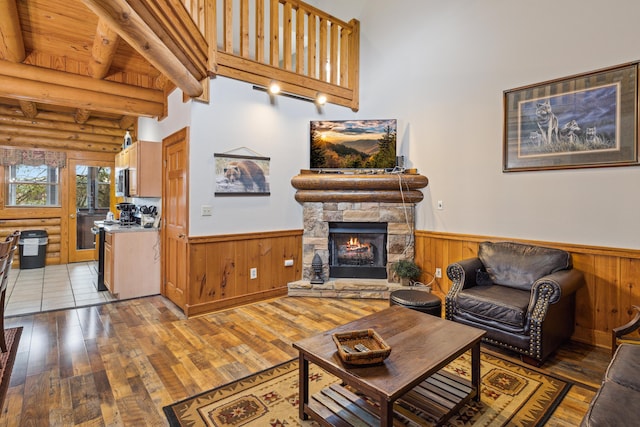 living room with beamed ceiling, wood-type flooring, a stone fireplace, and rustic walls