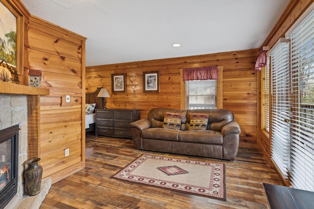 living room with dark wood-type flooring, a stone fireplace, and wood walls