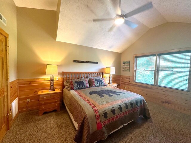 bedroom with ceiling fan, carpet floors, vaulted ceiling, a textured ceiling, and wooden walls