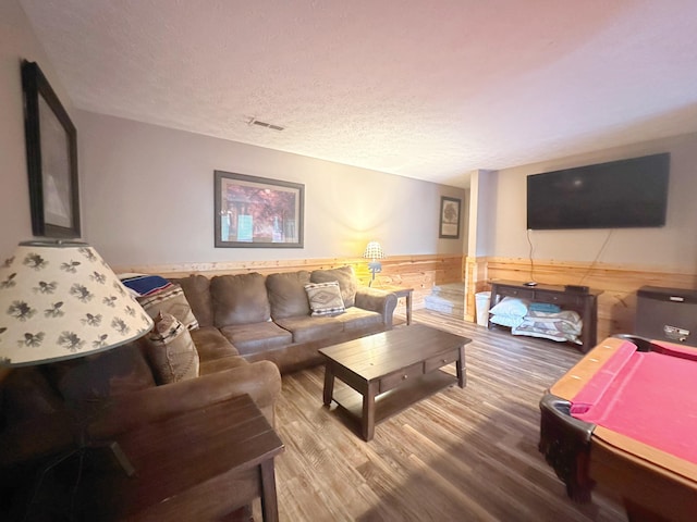 living room with a textured ceiling, hardwood / wood-style flooring, wooden walls, and billiards