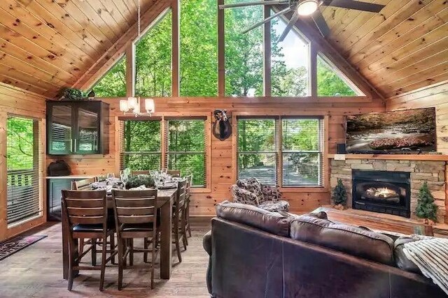 living room with wooden walls, wood-type flooring, high vaulted ceiling, wooden ceiling, and a stone fireplace