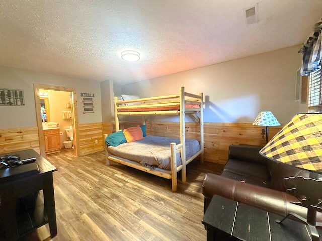 bedroom with hardwood / wood-style flooring, ensuite bathroom, a textured ceiling, and wooden walls