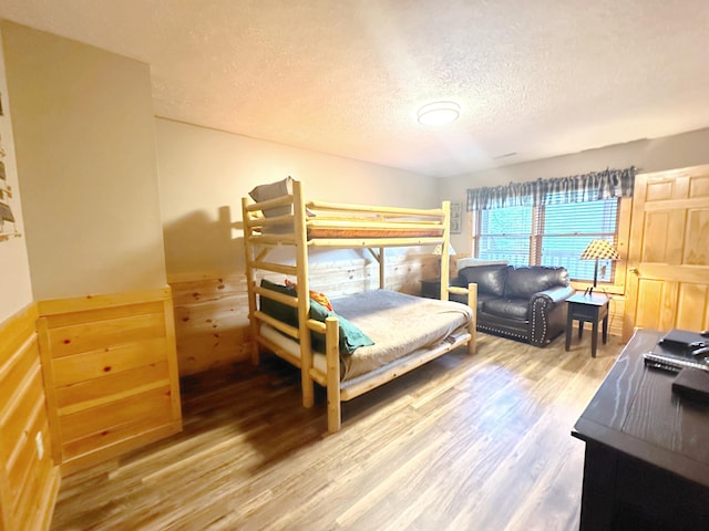 bedroom featuring hardwood / wood-style flooring, a textured ceiling, and wooden walls