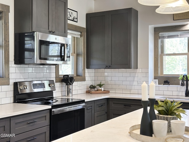 kitchen featuring stainless steel appliances, backsplash, gray cabinetry, and light countertops