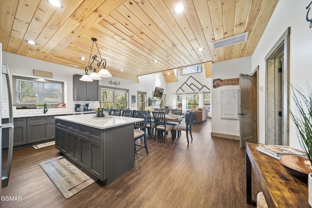 kitchen featuring visible vents, backsplash, gray cabinetry, a breakfast bar, and wooden ceiling