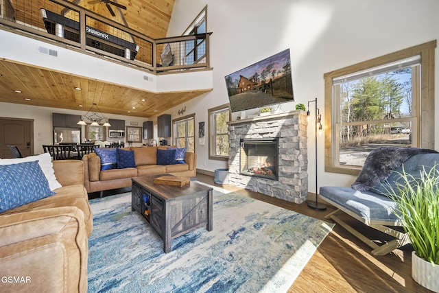 living area featuring wood finished floors, visible vents, a stone fireplace, a towering ceiling, and wooden ceiling