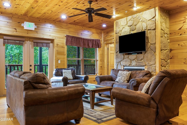 living room with ceiling fan, wood walls, light hardwood / wood-style floors, a fireplace, and wood ceiling