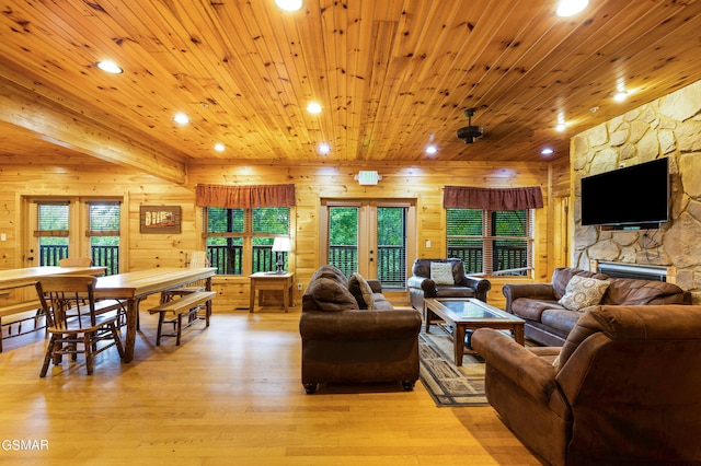 living room featuring light hardwood / wood-style flooring, a stone fireplace, wooden ceiling, and wood walls