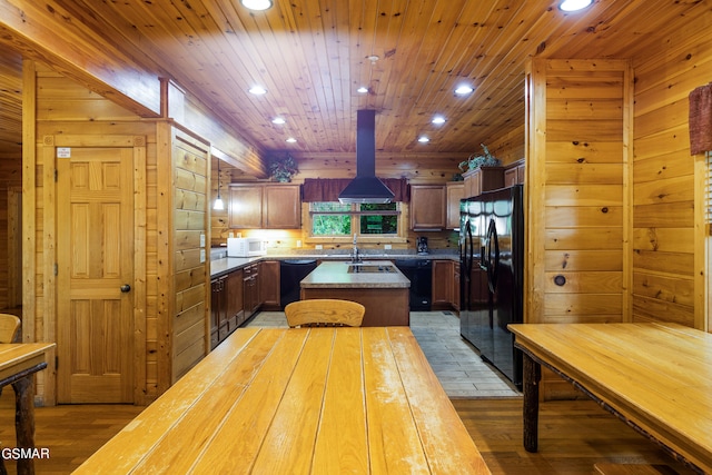 kitchen with island exhaust hood, wooden walls, black appliances, wood-type flooring, and a kitchen island