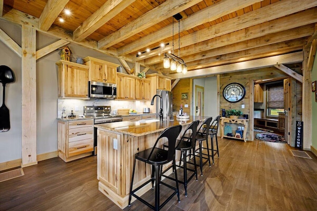 kitchen featuring an island with sink, light brown cabinetry, beam ceiling, appliances with stainless steel finishes, and sink