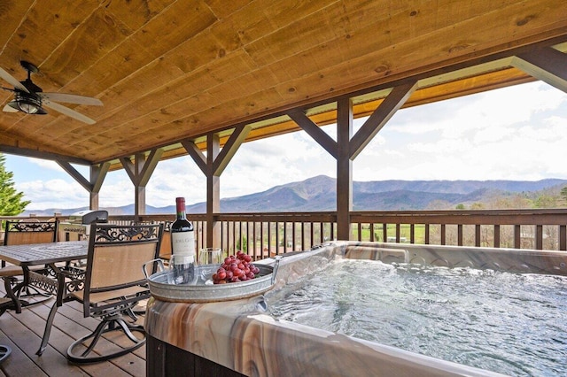 wooden deck with a mountain view, ceiling fan, and a hot tub