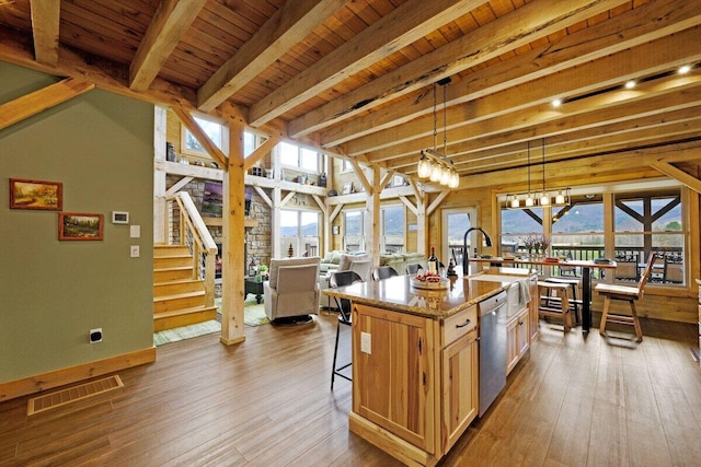 kitchen with light stone countertops, dishwasher, pendant lighting, an island with sink, and beam ceiling