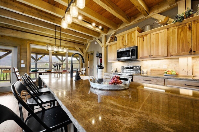 kitchen featuring wooden ceiling, beamed ceiling, a kitchen breakfast bar, hanging light fixtures, and appliances with stainless steel finishes