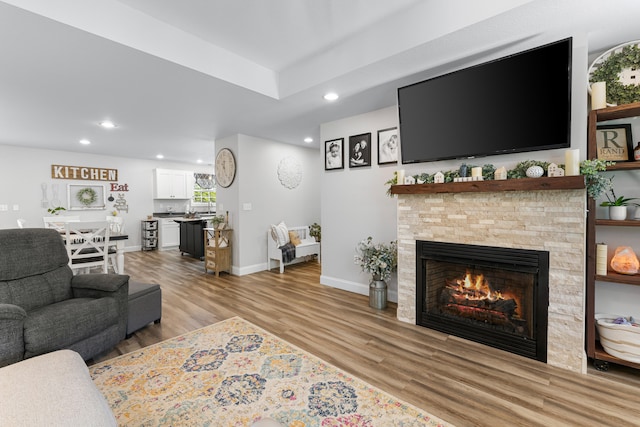 living room with recessed lighting, a stone fireplace, light wood-style flooring, and baseboards