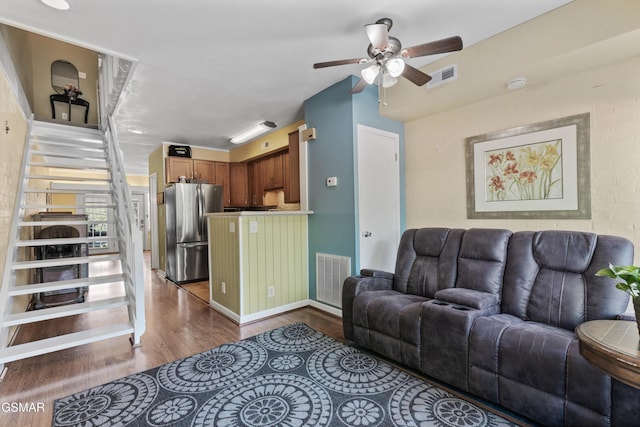 living area with dark wood-type flooring, a ceiling fan, and stairs