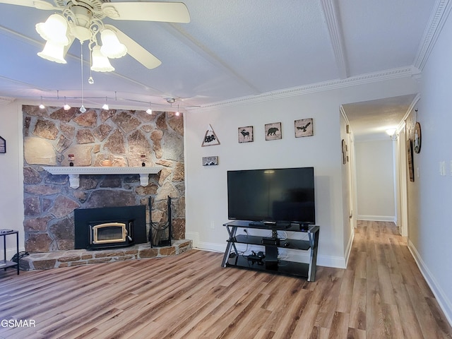 living room featuring crown molding, rail lighting, ceiling fan, light hardwood / wood-style floors, and a stone fireplace