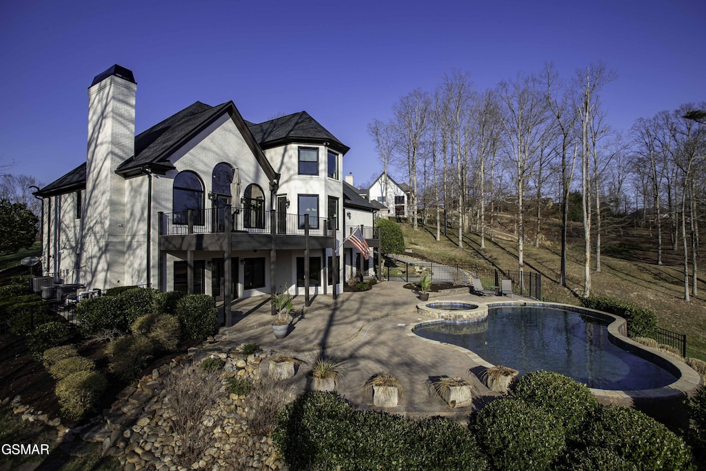 rear view of property featuring stucco siding, an outdoor pool, an in ground hot tub, a chimney, and a patio area