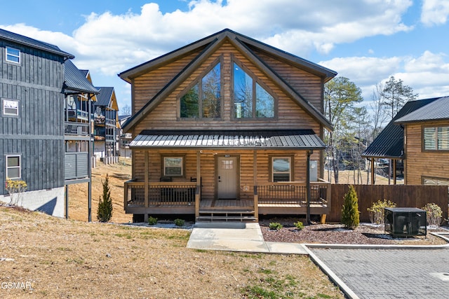 view of front of property with covered porch, metal roof, log veneer siding, and fence