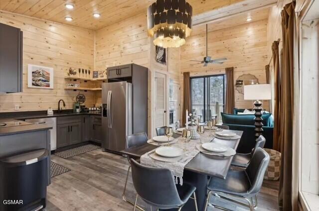 dining area with sink, wooden ceiling, wooden walls, hardwood / wood-style flooring, and a towering ceiling