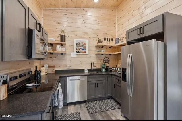 kitchen with stainless steel appliances, sink, wooden ceiling, and wooden walls